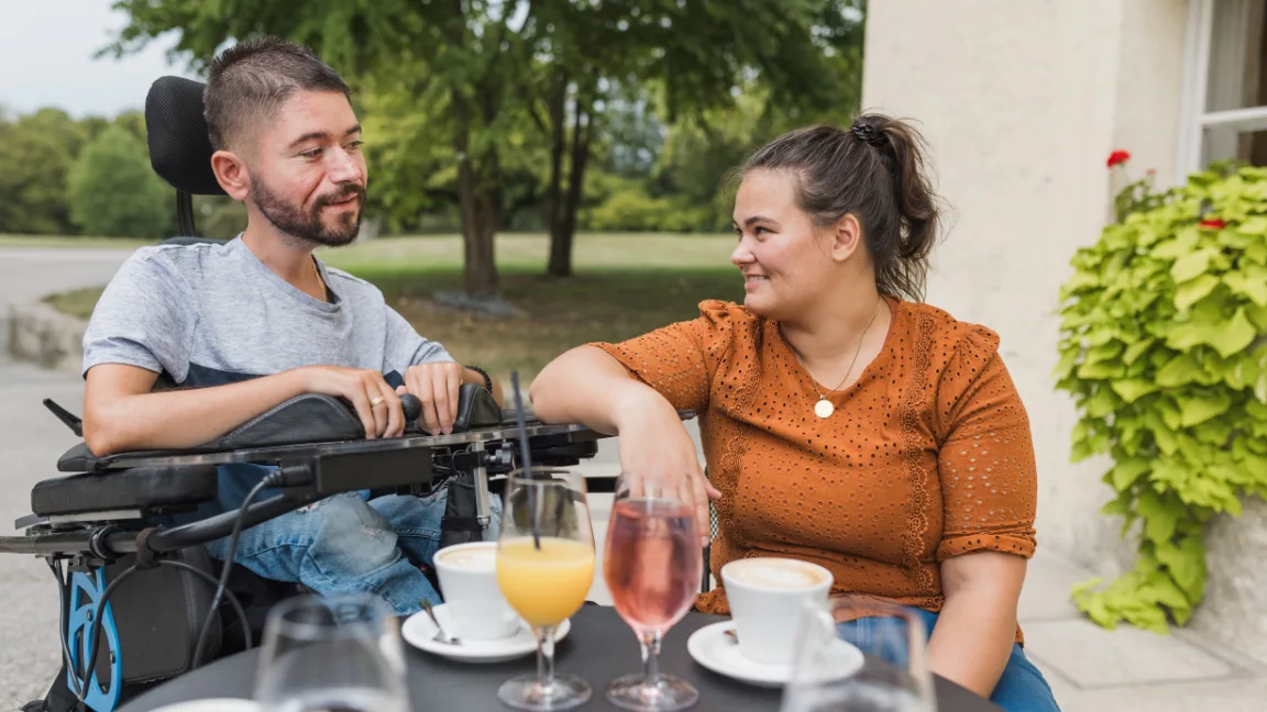 Disabled man in wheelchair at café with friend